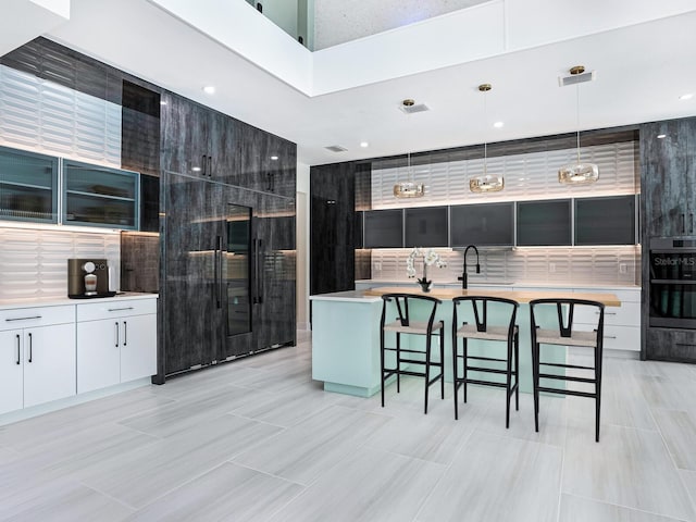 kitchen with a center island with sink, white cabinets, a breakfast bar area, and pendant lighting