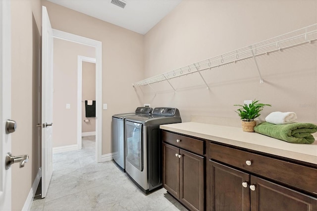 clothes washing area with washing machine and clothes dryer, cabinets, and light tile floors