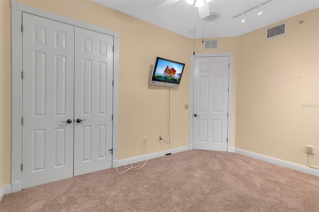 unfurnished bedroom featuring carpet flooring, rail lighting, a closet, and ceiling fan