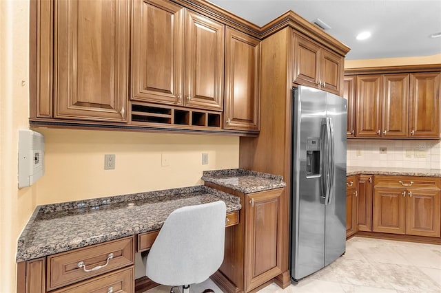 kitchen featuring built in desk, stainless steel refrigerator with ice dispenser, dark stone counters, and tasteful backsplash