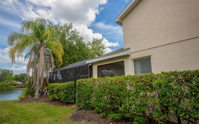 view of side of home featuring a lanai, a water view, a lawn, and stucco siding