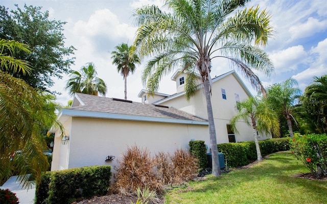 view of side of home featuring roof with shingles, central AC unit, a lawn, and stucco siding