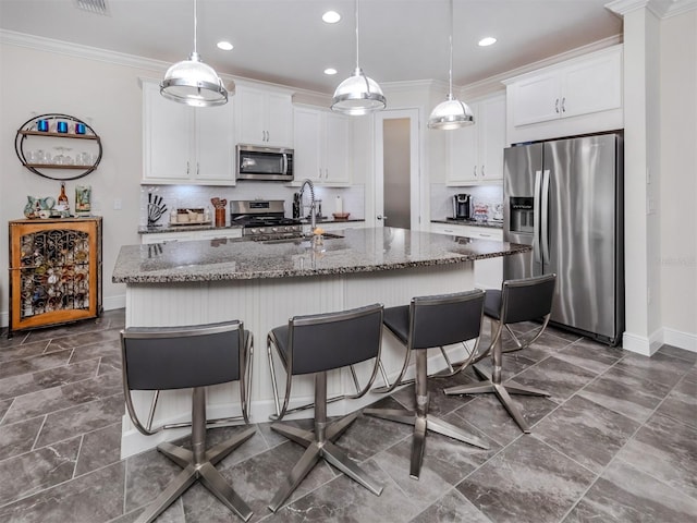 kitchen with white cabinetry, backsplash, stainless steel appliances, hanging light fixtures, and a center island with sink