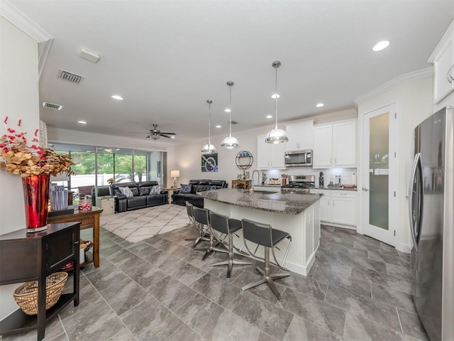 kitchen with a breakfast bar area, a kitchen island with sink, stainless steel appliances, white cabinets, and dark stone counters