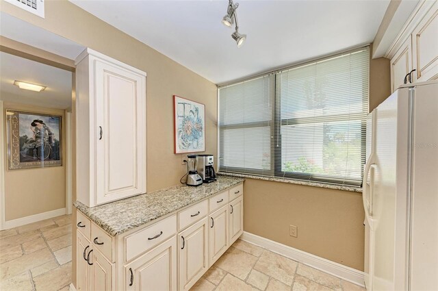 kitchen featuring light stone counters and white fridge with ice dispenser