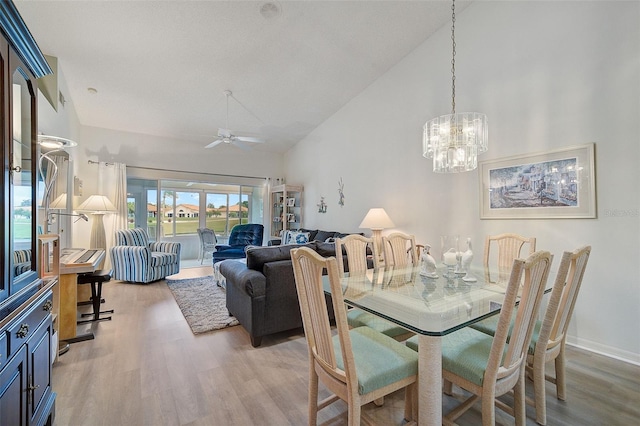 dining area featuring high vaulted ceiling, light hardwood / wood-style flooring, and ceiling fan with notable chandelier