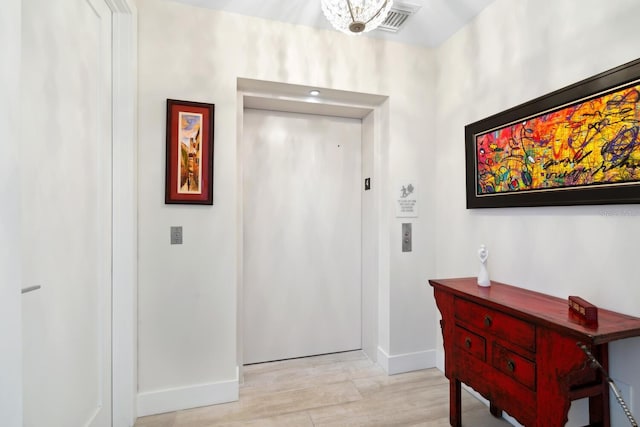 entryway with light wood-type flooring, elevator, and a chandelier