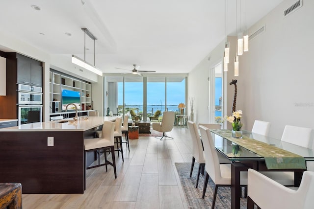 kitchen featuring double oven, ceiling fan, hanging light fixtures, and light wood-type flooring