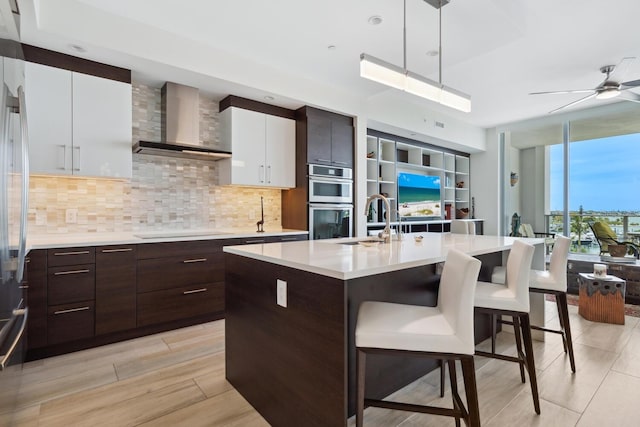 kitchen featuring white cabinetry, wall chimney exhaust hood, decorative light fixtures, black electric cooktop, and a center island with sink