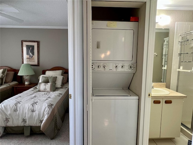 clothes washing area featuring a textured ceiling, stacked washer / drying machine, sink, and ornamental molding