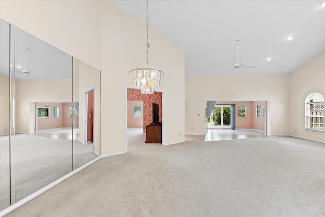 unfurnished living room with a high ceiling, ceiling fan with notable chandelier, and light colored carpet