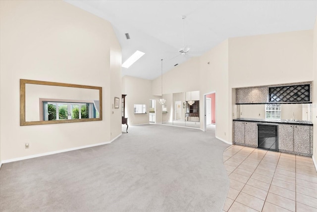 unfurnished living room with light tile floors, beverage cooler, high vaulted ceiling, and ceiling fan with notable chandelier