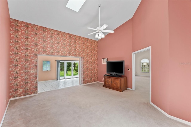 unfurnished living room featuring a skylight, ceiling fan, light colored carpet, and high vaulted ceiling