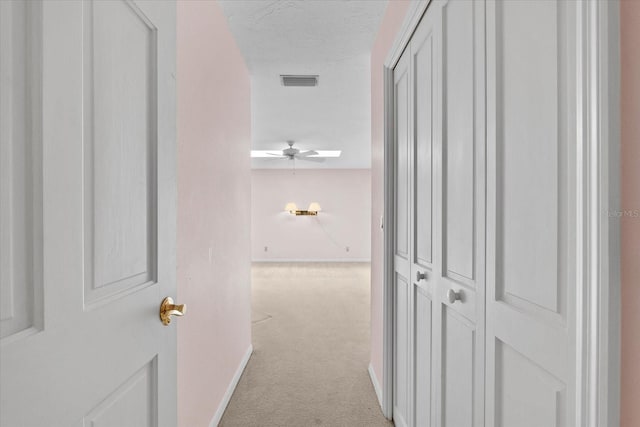 hallway with light colored carpet and a textured ceiling