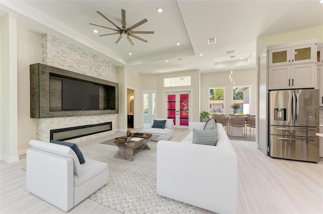 living room with a raised ceiling, a fireplace, and ceiling fan