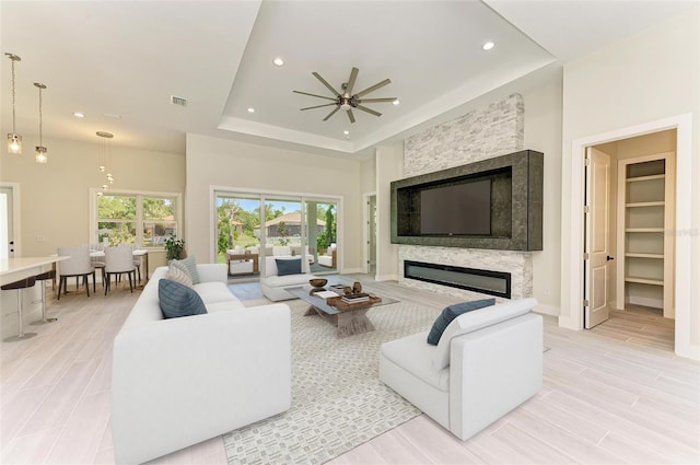 living room with plenty of natural light, a tray ceiling, ceiling fan, and a fireplace