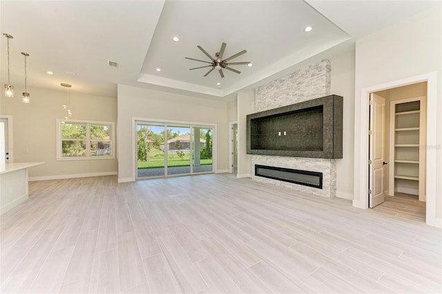 unfurnished living room featuring light hardwood / wood-style floors, a fireplace, ceiling fan, and a tray ceiling