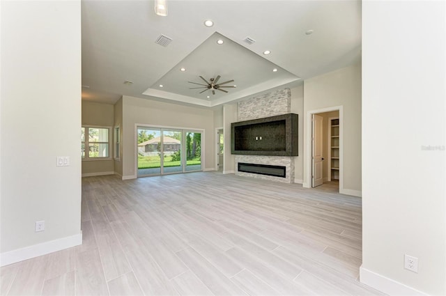 unfurnished living room featuring a raised ceiling, light hardwood / wood-style floors, a fireplace, and ceiling fan