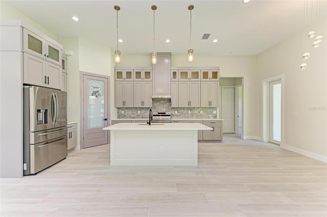 kitchen with hanging light fixtures, appliances with stainless steel finishes, sink, a center island with sink, and tasteful backsplash