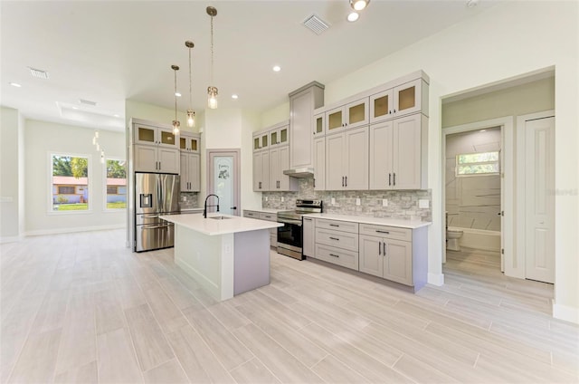 kitchen with plenty of natural light, hanging light fixtures, stainless steel appliances, and a kitchen island with sink