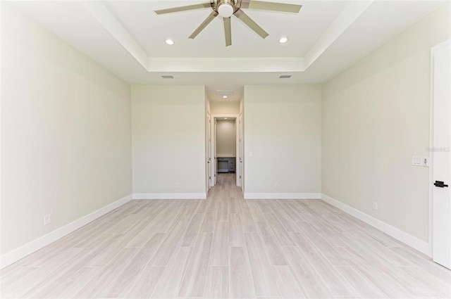 empty room featuring light hardwood / wood-style flooring, a raised ceiling, and ceiling fan