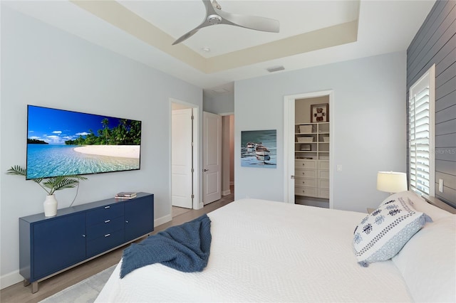 bedroom with ceiling fan, wood-type flooring, a tray ceiling, a walk in closet, and a closet