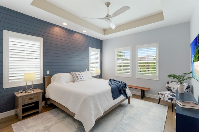 bedroom featuring hardwood / wood-style flooring, ceiling fan, wood walls, and a tray ceiling