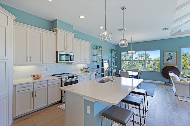 kitchen with tasteful backsplash, stainless steel appliances, sink, white cabinetry, and an island with sink