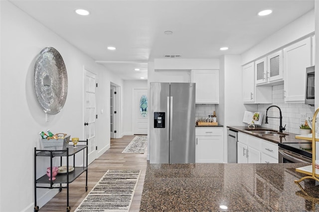 kitchen with light hardwood / wood-style flooring, appliances with stainless steel finishes, dark stone countertops, backsplash, and sink