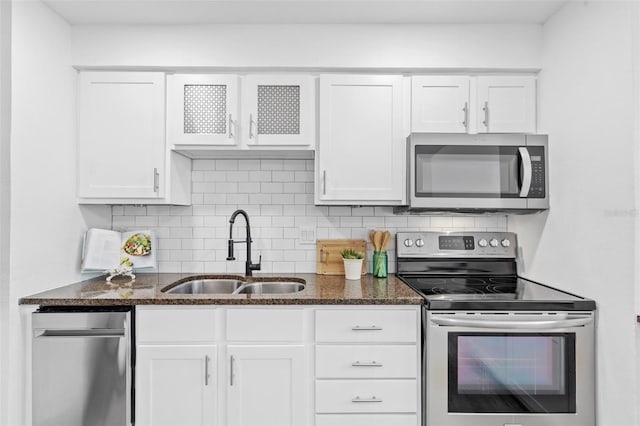 kitchen featuring appliances with stainless steel finishes, sink, white cabinets, and dark stone counters