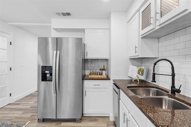 kitchen with appliances with stainless steel finishes, backsplash, white cabinets, light hardwood / wood-style flooring, and sink