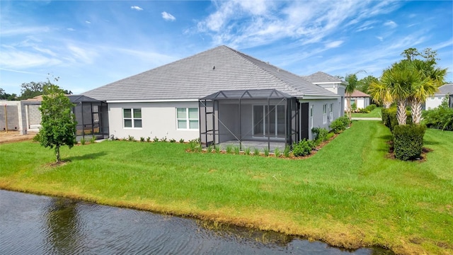 back of property with glass enclosure, a yard, and a water view