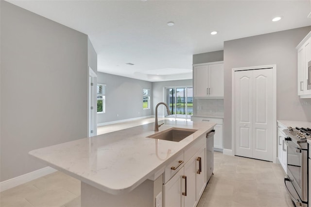 kitchen with a kitchen island with sink, sink, light stone countertops, appliances with stainless steel finishes, and white cabinetry