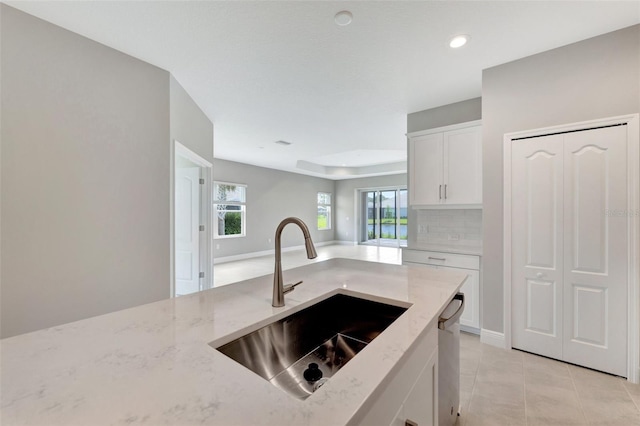 kitchen featuring light stone countertops, backsplash, sink, dishwasher, and white cabinetry