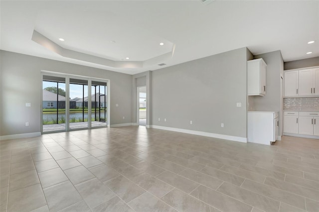 unfurnished living room featuring a water view, light tile patterned floors, and a tray ceiling