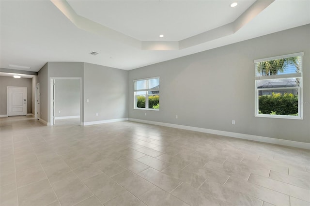 unfurnished room with light tile patterned floors and a tray ceiling