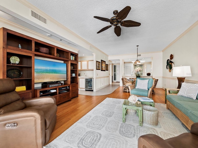 living room featuring crown molding, light hardwood / wood-style flooring, ceiling fan, a textured ceiling, and beverage cooler