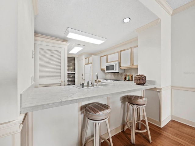 kitchen with tile counters, a kitchen breakfast bar, kitchen peninsula, light hardwood / wood-style floors, and white appliances