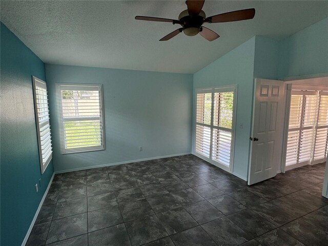 tiled empty room featuring ceiling fan, vaulted ceiling, and a healthy amount of sunlight