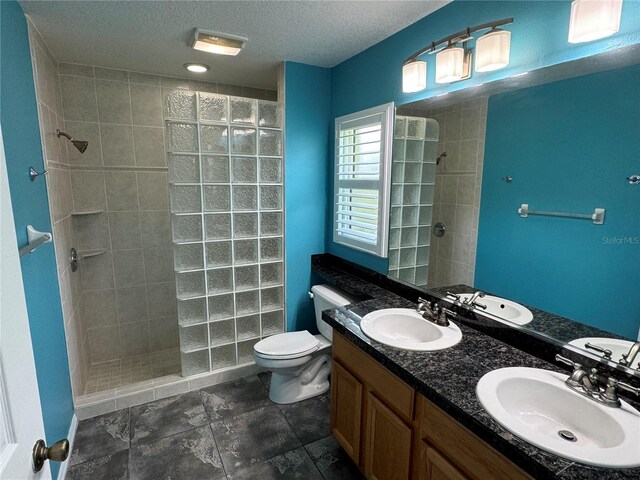 bathroom with a tile shower, tile patterned floors, a textured ceiling, vanity, and toilet