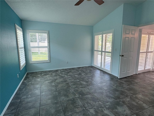 empty room featuring ceiling fan, dark tile patterned floors, a textured ceiling, and lofted ceiling