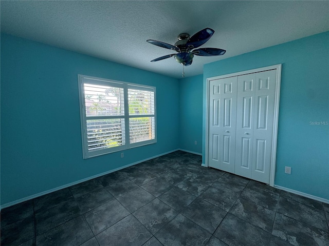 unfurnished bedroom featuring ceiling fan, dark tile patterned flooring, a closet, and a textured ceiling