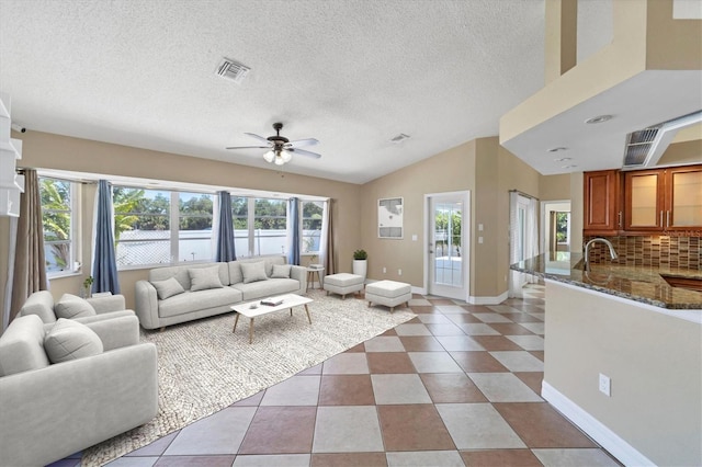 living room featuring ceiling fan, light tile floors, sink, vaulted ceiling, and a textured ceiling