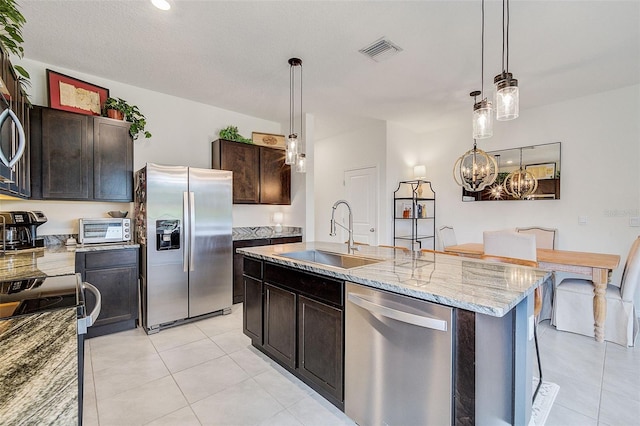 kitchen with light stone countertops, sink, stainless steel appliances, dark brown cabinets, and pendant lighting