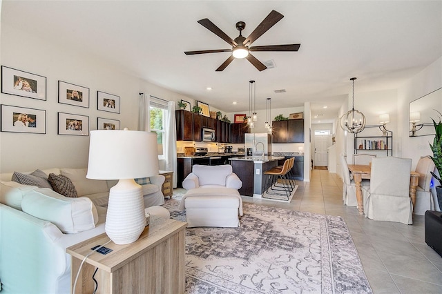 tiled living room featuring ceiling fan with notable chandelier and sink