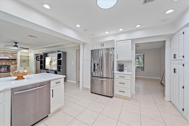 kitchen featuring a brick fireplace, ceiling fan, appliances with stainless steel finishes, backsplash, and white cabinetry