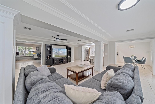 living room featuring crown molding, decorative columns, light tile flooring, a tray ceiling, and ceiling fan with notable chandelier