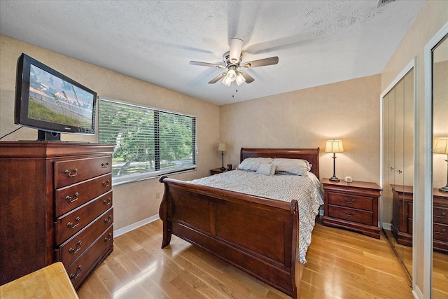 bedroom featuring ceiling fan, a closet, light hardwood / wood-style flooring, and a textured ceiling