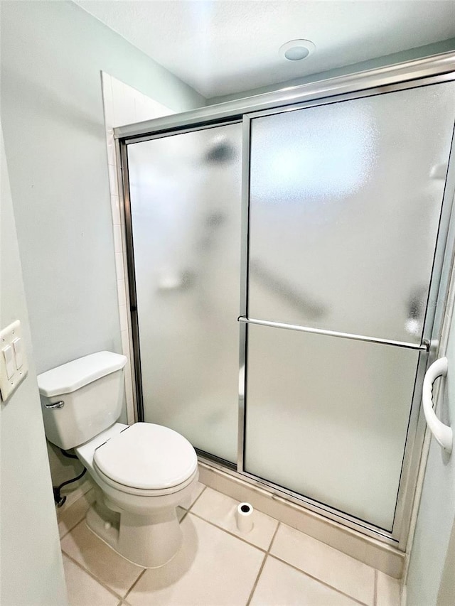 bathroom featuring tile flooring, a shower with door, and toilet