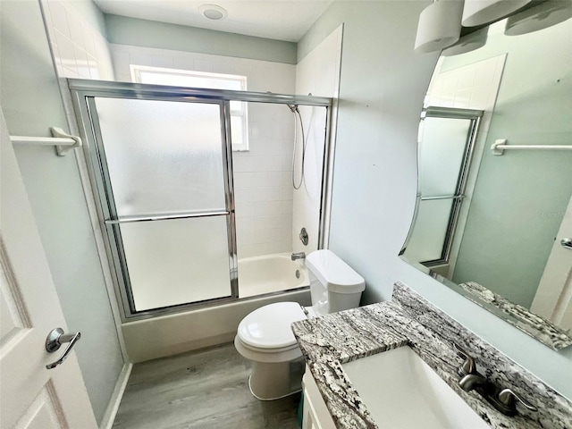 full bathroom featuring hardwood / wood-style floors, vanity with extensive cabinet space, toilet, and bath / shower combo with glass door